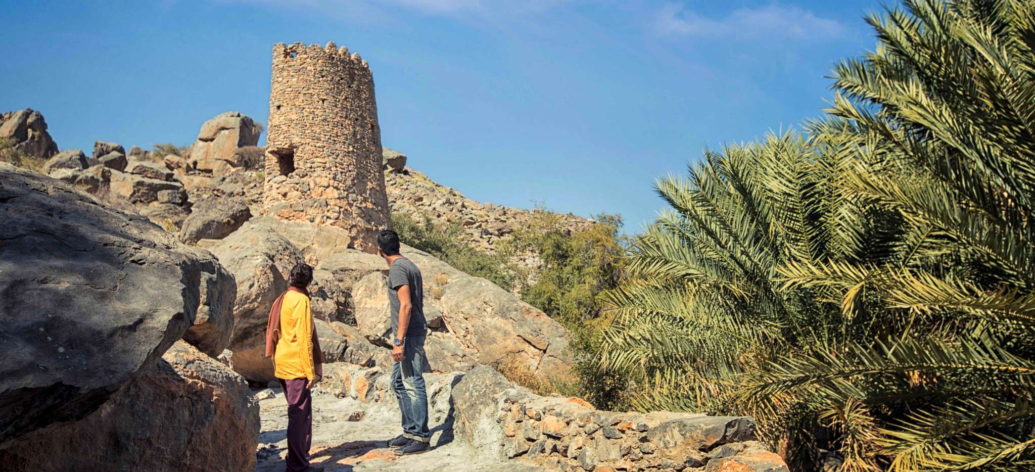 Paar betrachtet einen verfallenen Steinturm auf einem Berg im Dorf Misfat im Oman