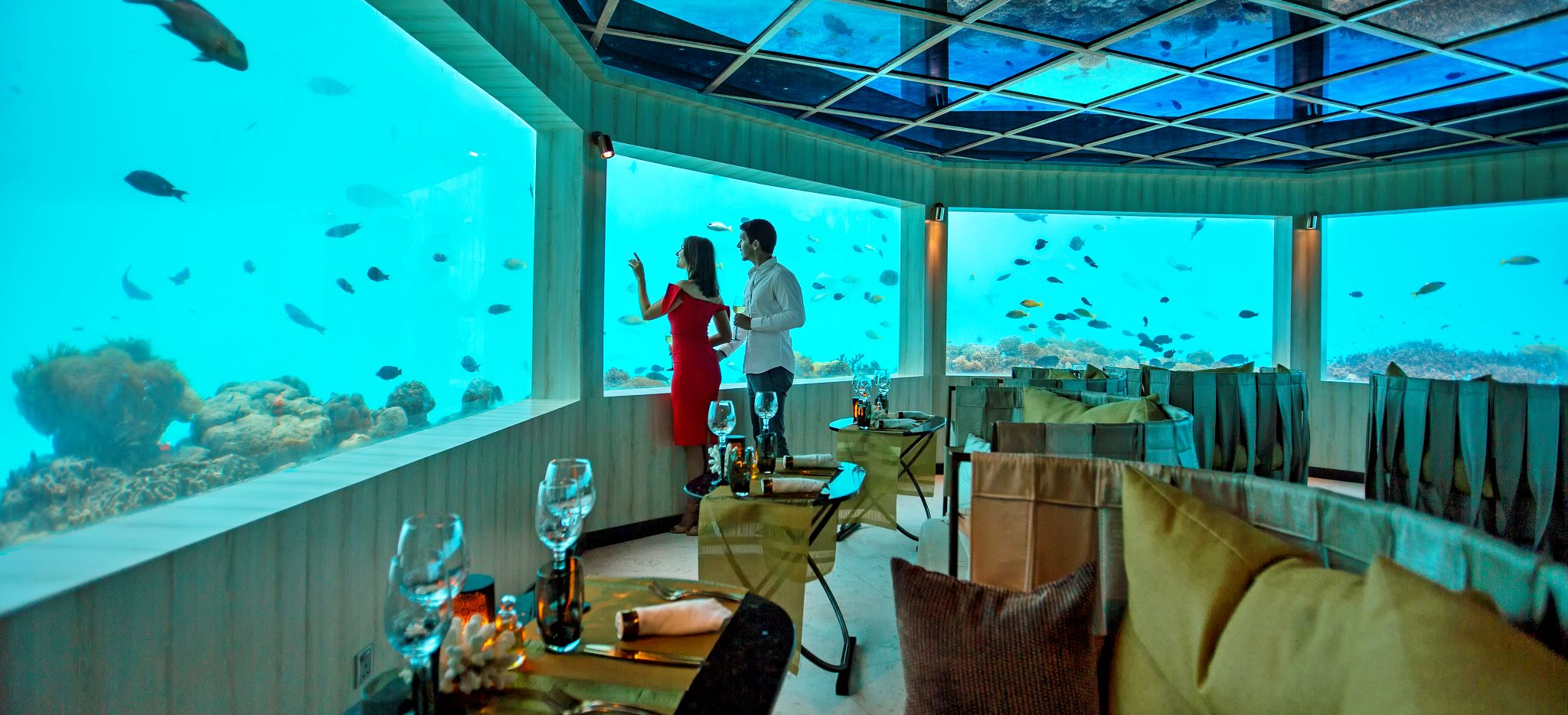 Ein paar betrachtet Fische durch ein Fenster in einem Unterwasser Restaurant im Hotel OZEN, Malediven