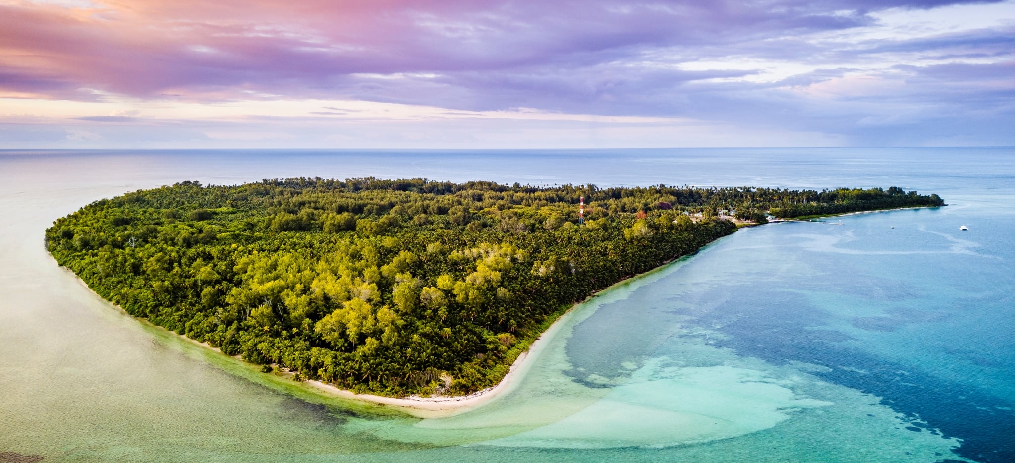 Luftaufnahme der Insel Alphonse während eines Sonnenunterganges, mit türkisem Meer und rosa Wolken